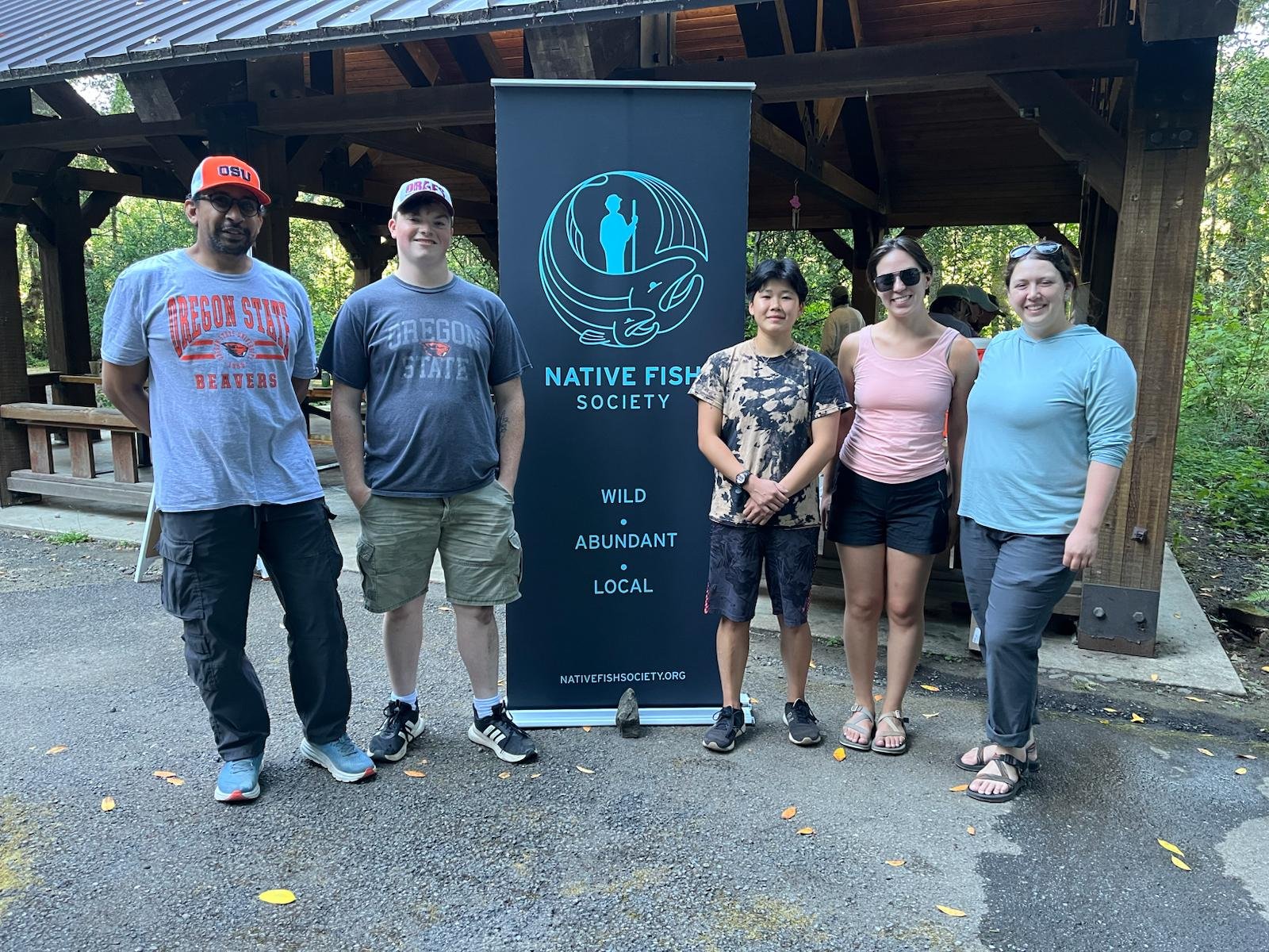 A group of five people standing beside a Native Fish Society banner at an outdoor pavilion.