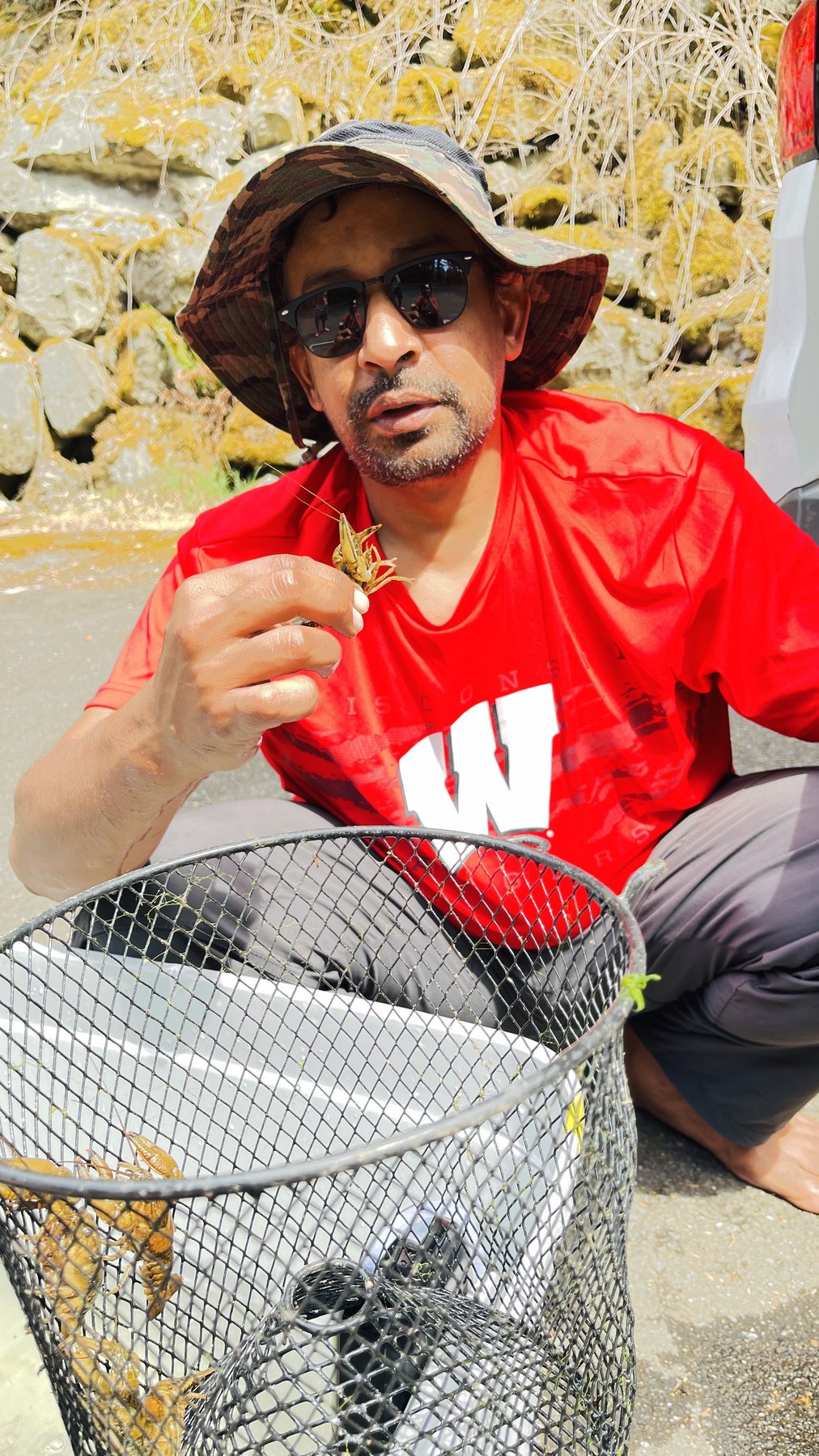 A researcher crouches beside a wire mesh trap holding one crayfish, with several more visible inside the trap.