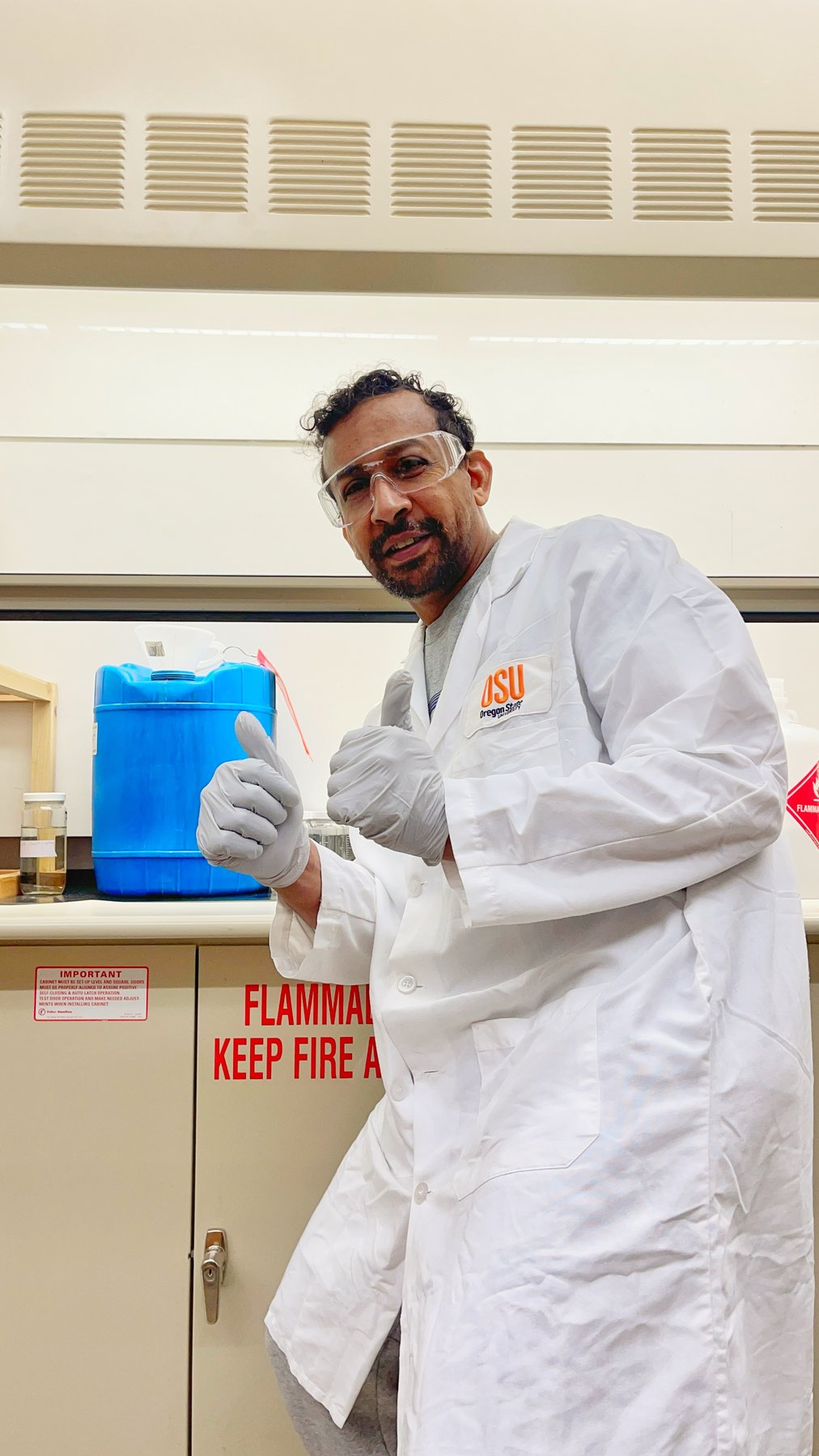 A researcher wearing a lab coat and safety glasses in a laboratory.