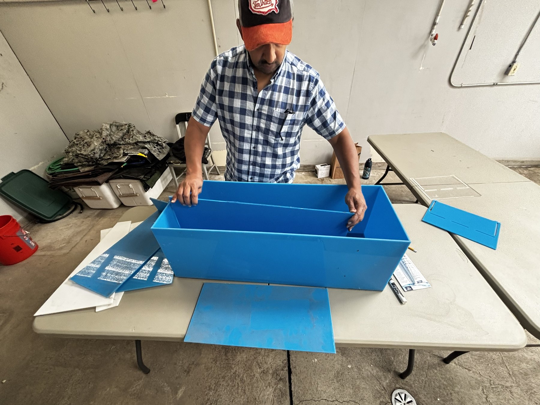 A researcher assembling a custom blue rectangular experimental tank with a center divider on a workbench.